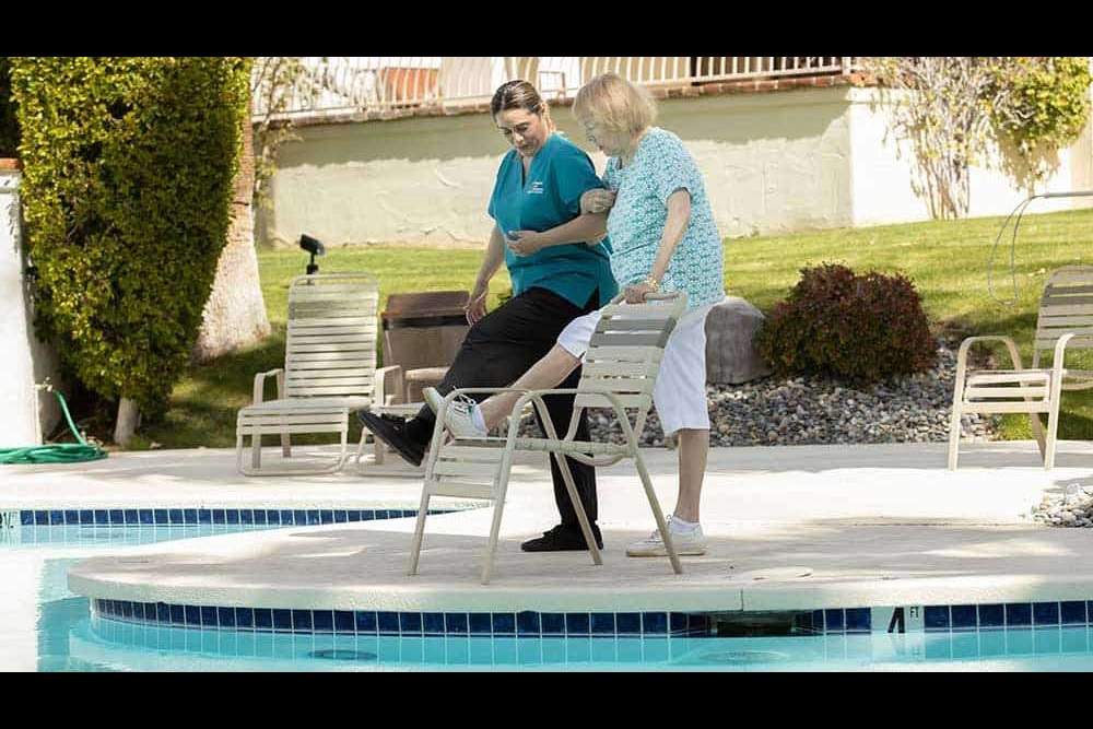 Caregiver exercising with senior by swimming pool