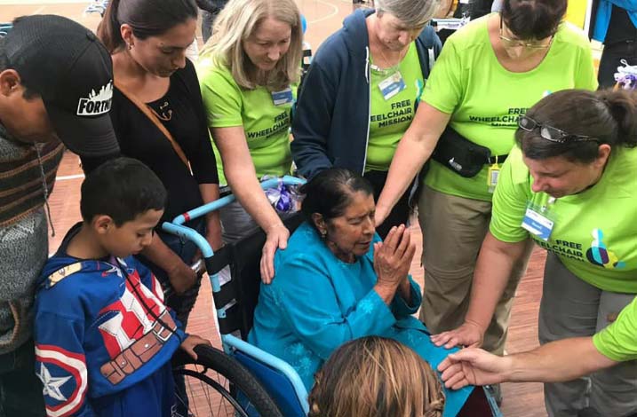 A number of caregivers praying with an Ecuadorian woman in a wheelchair.