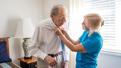 RAH-Website-Heroes-011720226-Mobile-420x236 Female caregiver helping client put on his tie.