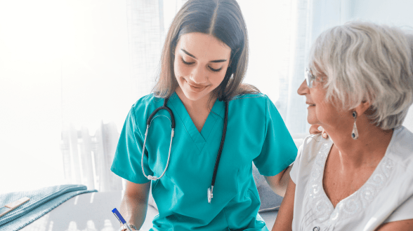 A female nurse with a stethoscope conversing with an elderly female patient.