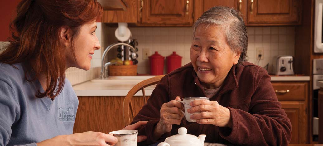 A caregiver smiles at her client over a cup of tea.