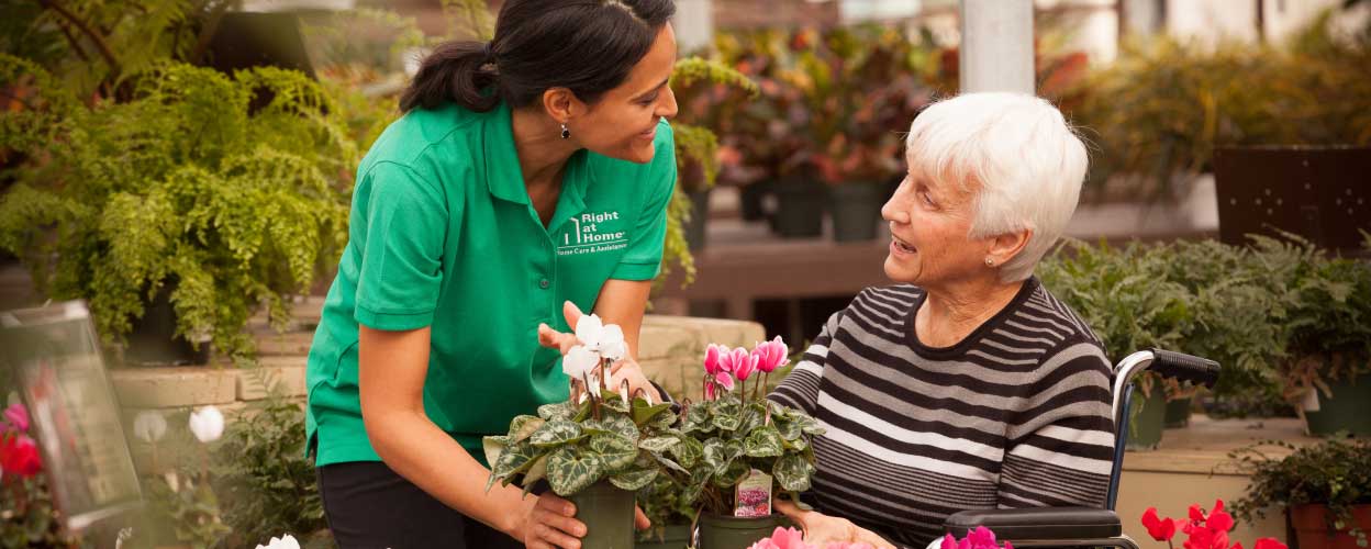 A female caregiver talking to an elderly woman in a wheelchair at a flower garden