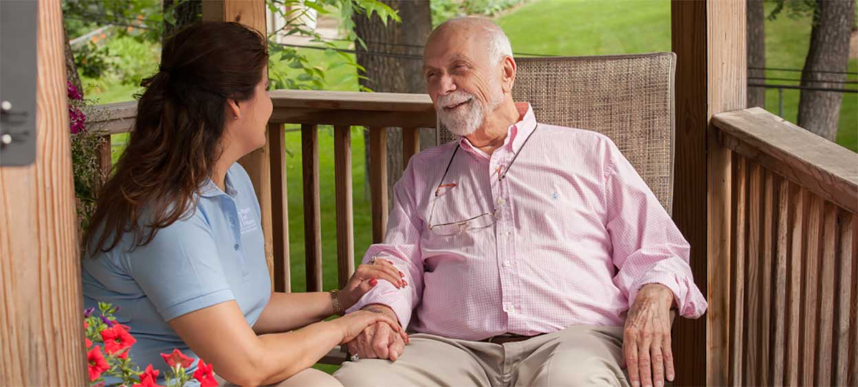 A caregiver comforts a patient sitting in a chair.