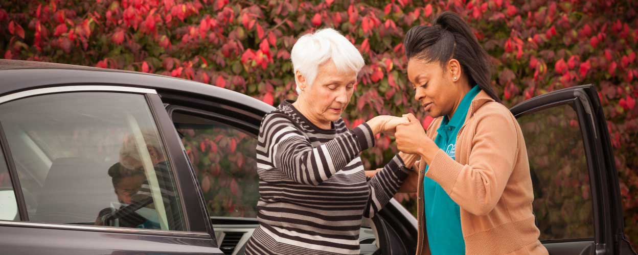 A patient being helped out of a car by her caregiver.