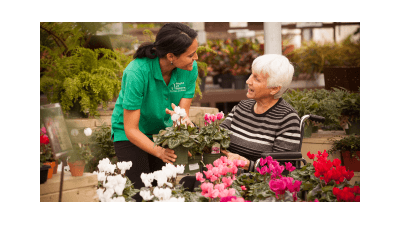 A female caregiver talking to an elderly woman in a wheelchair at a flower garden