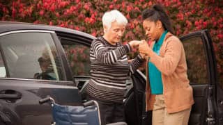 A patient being helped out of a car by her caregiver.