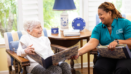 female caregiver and female senior client looking at photo albums while sitting down