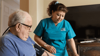 A female nurse assists with a blood pressure device attached to a male patient's arm.