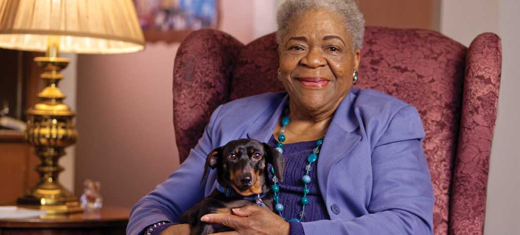 An elderly woman sitting comfortably with a dog on a single sofa chair