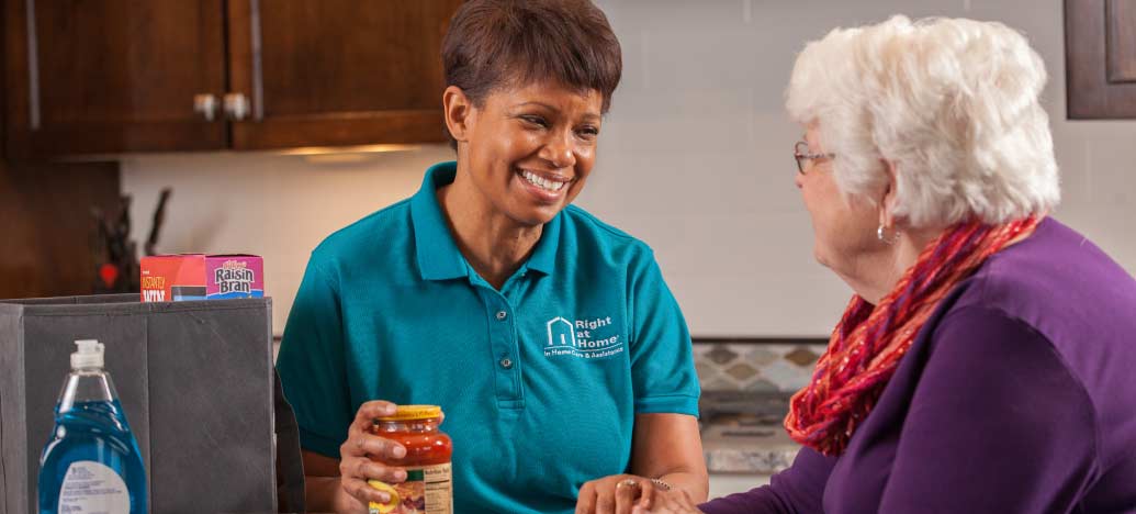 A caregiver talks to her patient, an elderly woman, while they unpack groceries.